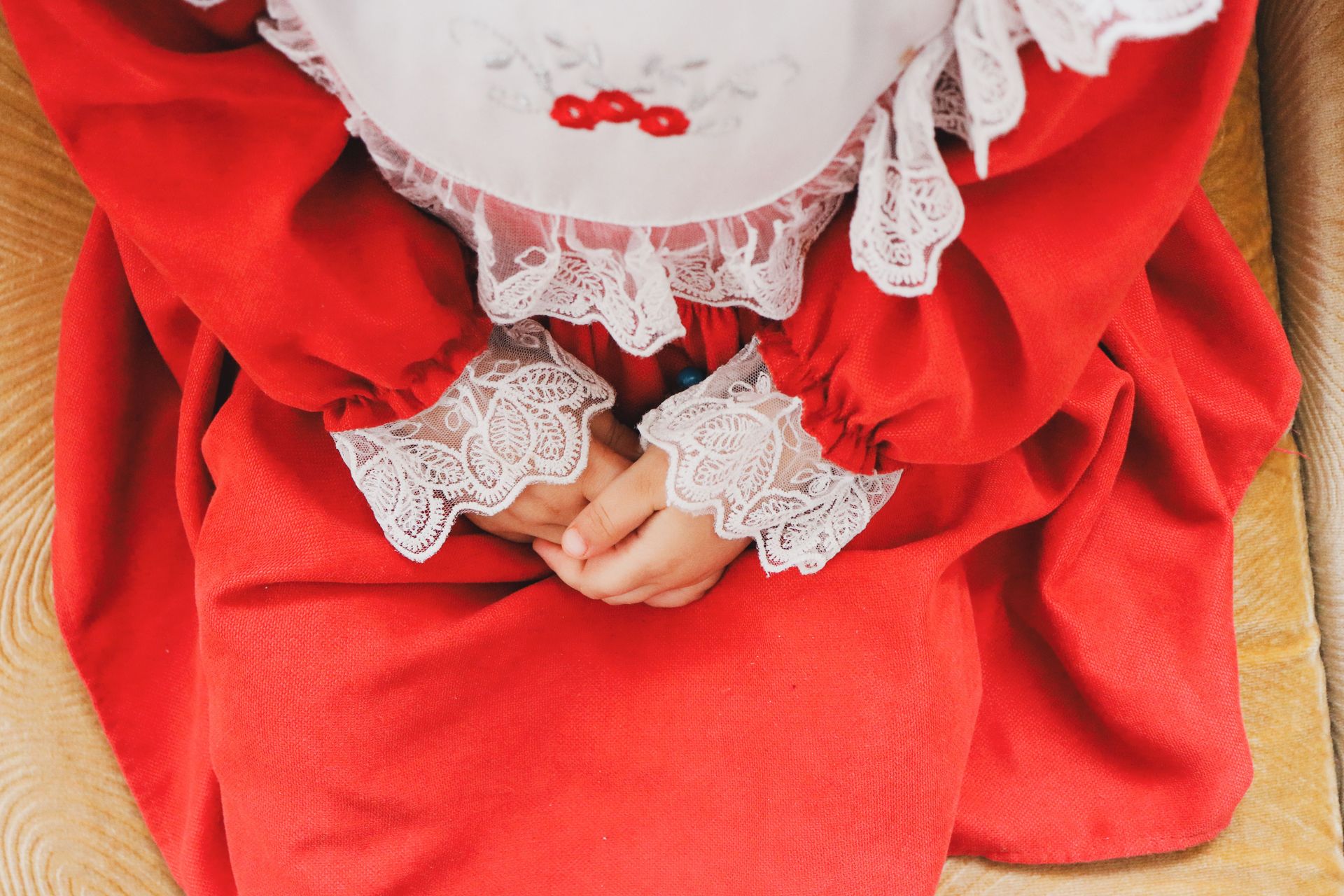 Top view of a child in a red dress with lace detailing, hands clasped.